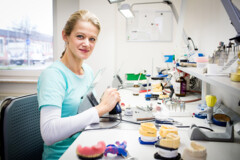 KI generiert: Eine Person arbeitet lächelnd in einem zahnmedizinischen Labor an Zahnmodellen.