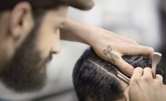 Mann scheitelt Haar eines anderen Mannes. Tatoowierung einer Schere auf der linken Hand des Friseurs