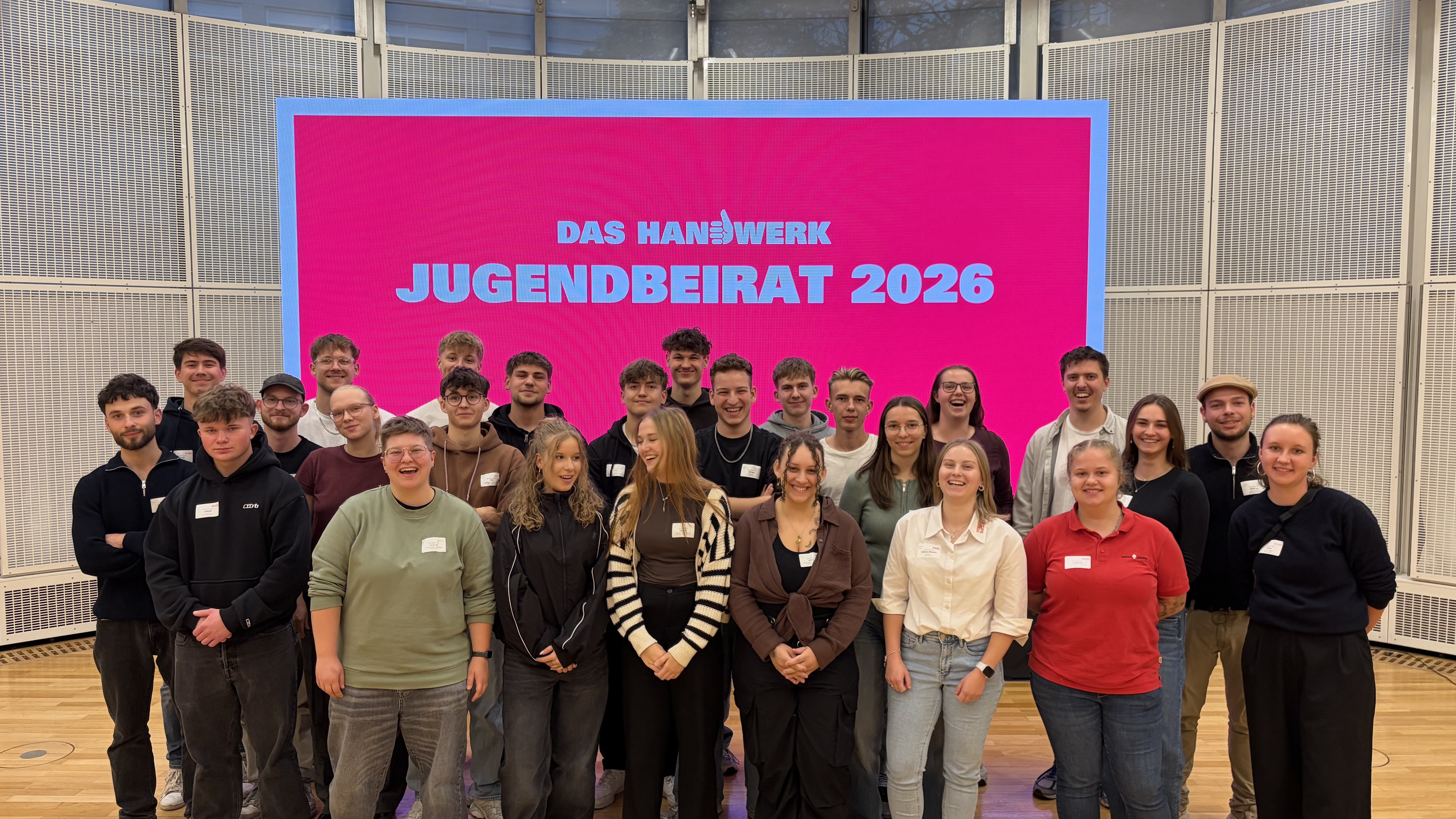 KI generiert: Das Bild zeigt eine Gruppe von Menschen, die vor einem pinken Banner mit der Aufschrift "DAS HANDWERK JUGENDBEIRAT 2026" stehen.