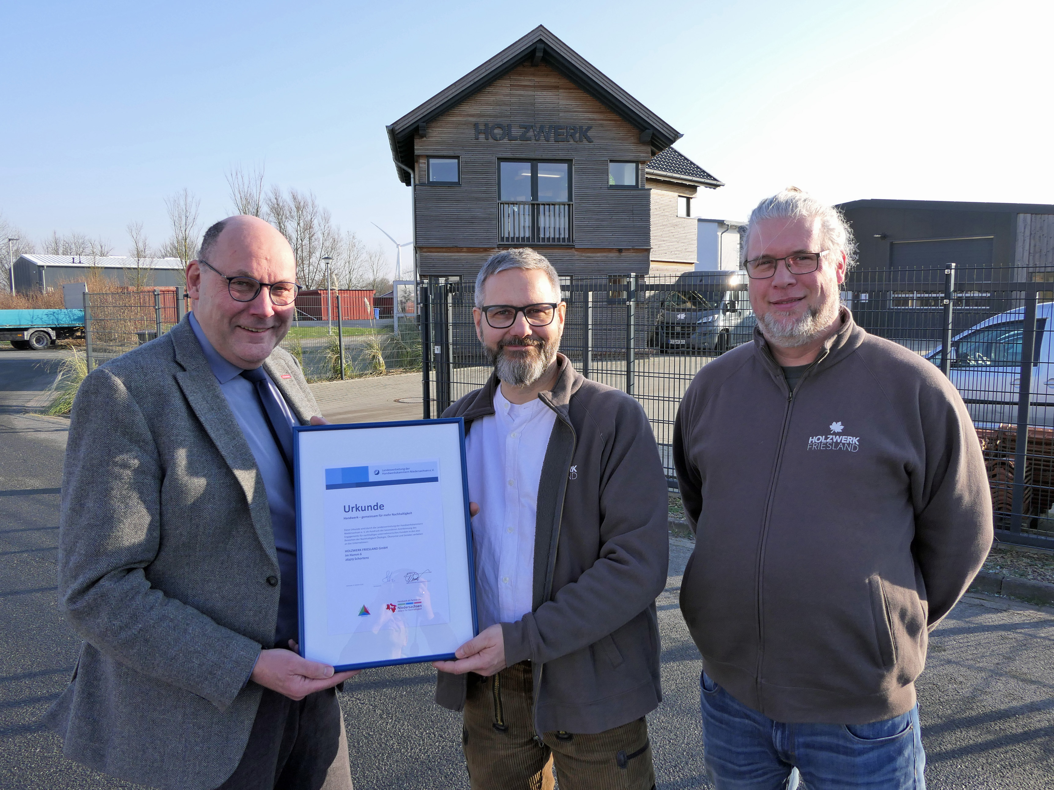 KI generiert: Drei Männer stehen vor einem Gebäude mit der Aufschrift "HOLZWERK" und halten ein gerahmtes Zertifikat.