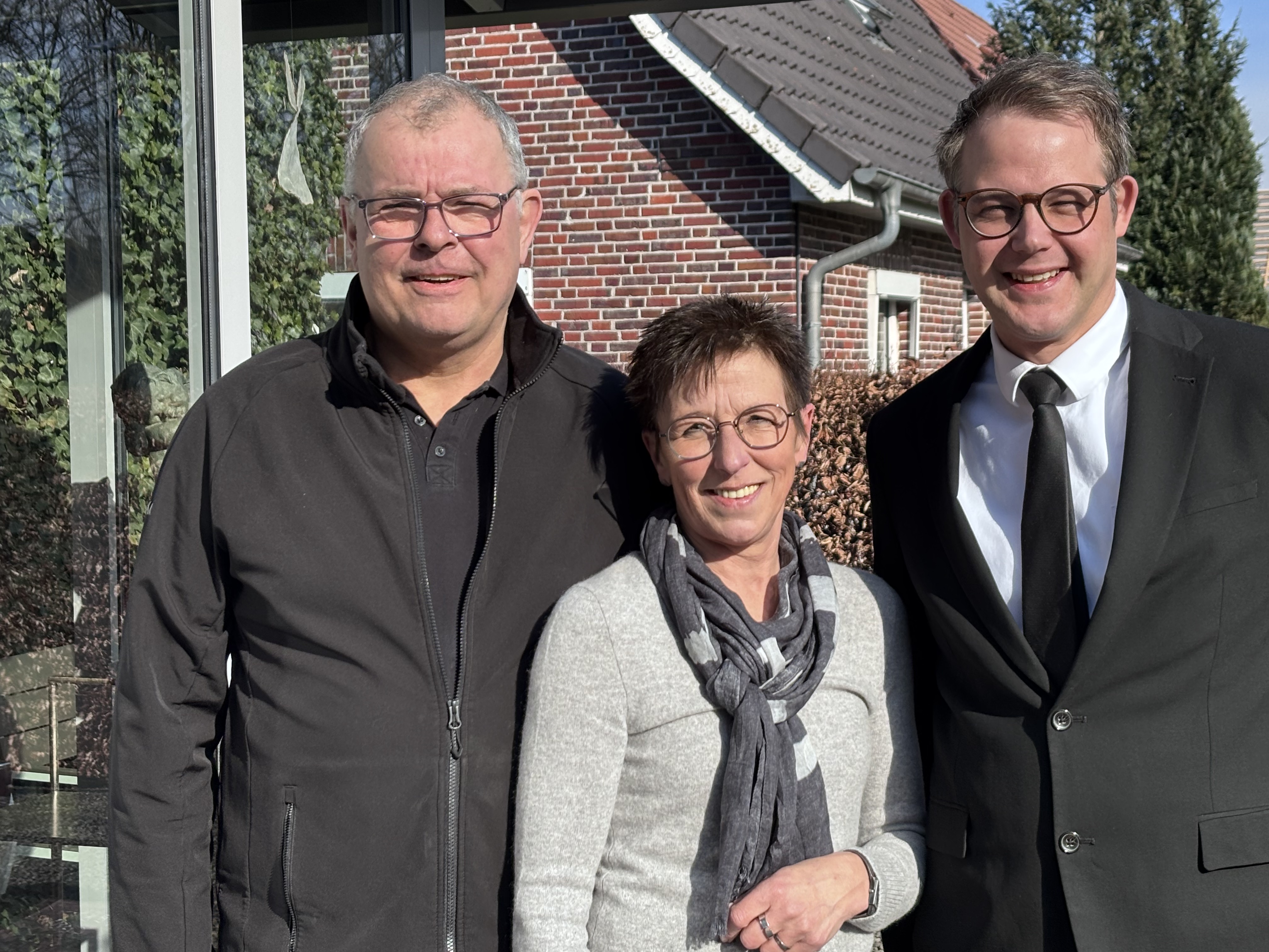 Fünf Männer posieren nebeneinander in einem Raum mit großen Fenstern, und einer trägt Bäckerkleidung.