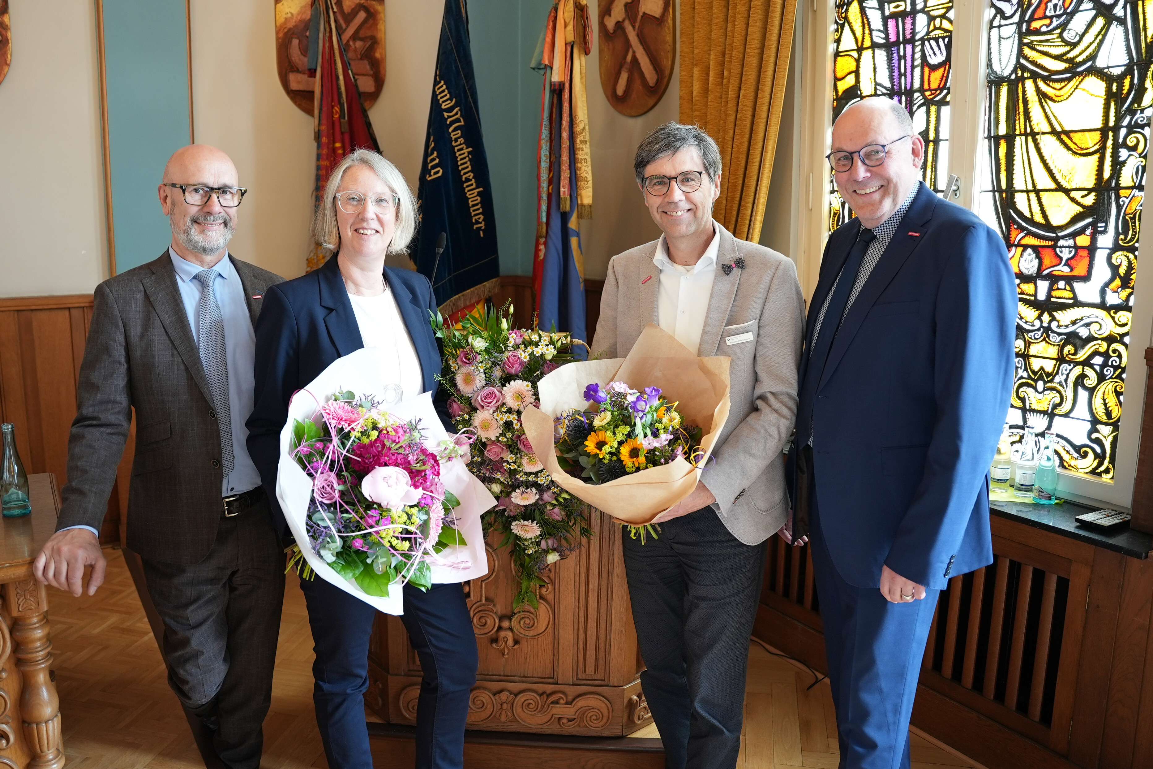 KI generiert: Vier Personen posieren in einem feierlichen Raum mit großen Blumensträußen.