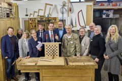 KI generiert: Eine Gruppe von Menschen steht in einer Werkstatt um ein Schachbrett herum.