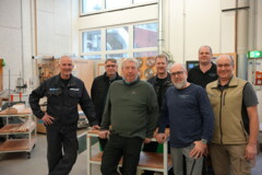 KI generiert: Eine Gruppe von acht Männern steht in einer Werkstatt vor Holzbearbeitungsmaschinen.