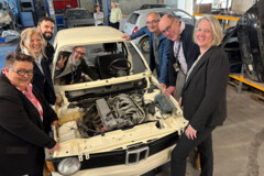 KI generiert: Eine Gruppe von Menschen versammelt sich um ein Auto ohne Motorhaube in einer Werkstatt.