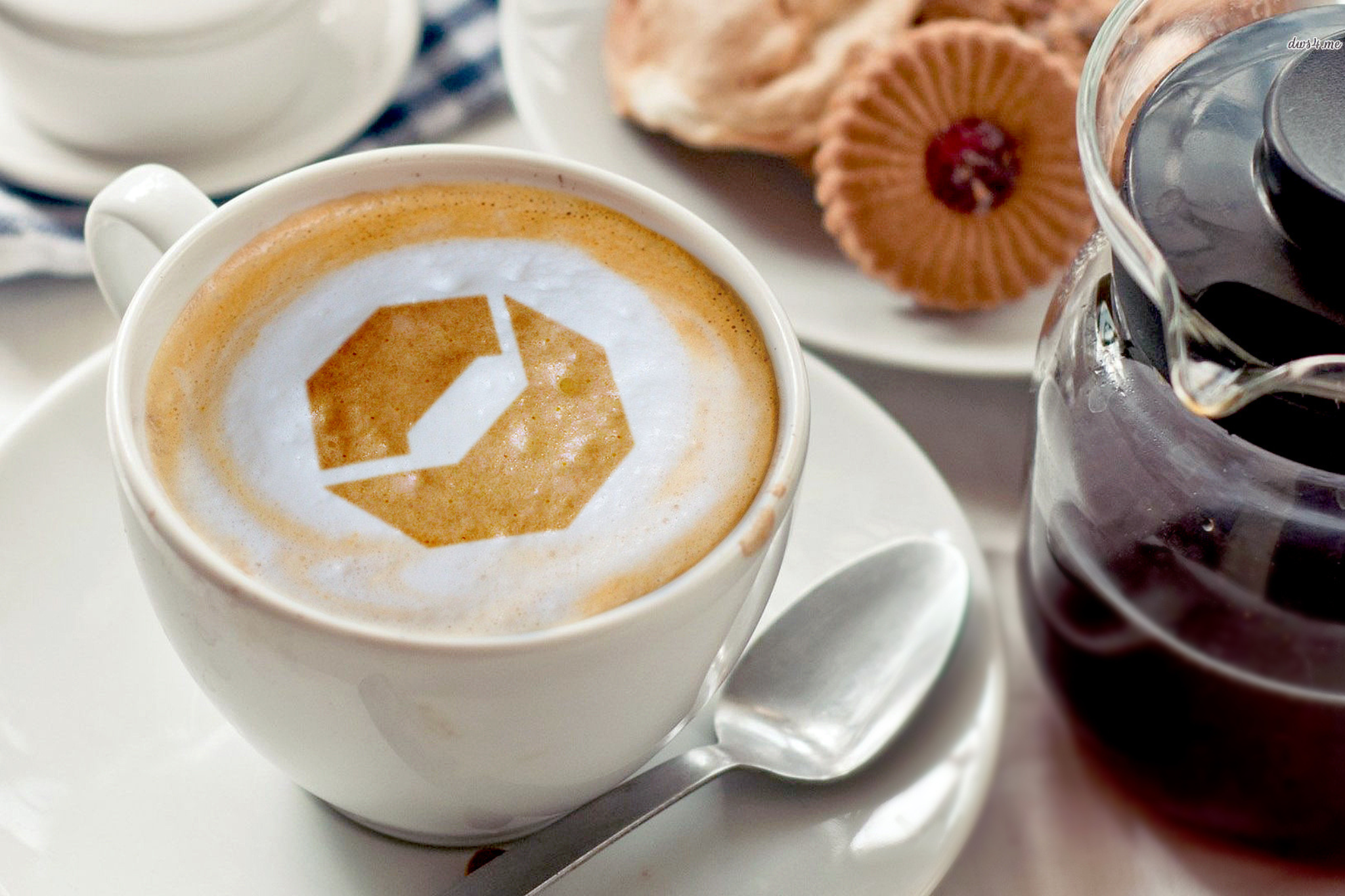 KI generiert: Eine Tasse Cappuccino mit einem dekorativen Muster im Milchschaum neben einer Kanne Kaffee und Gebäck.