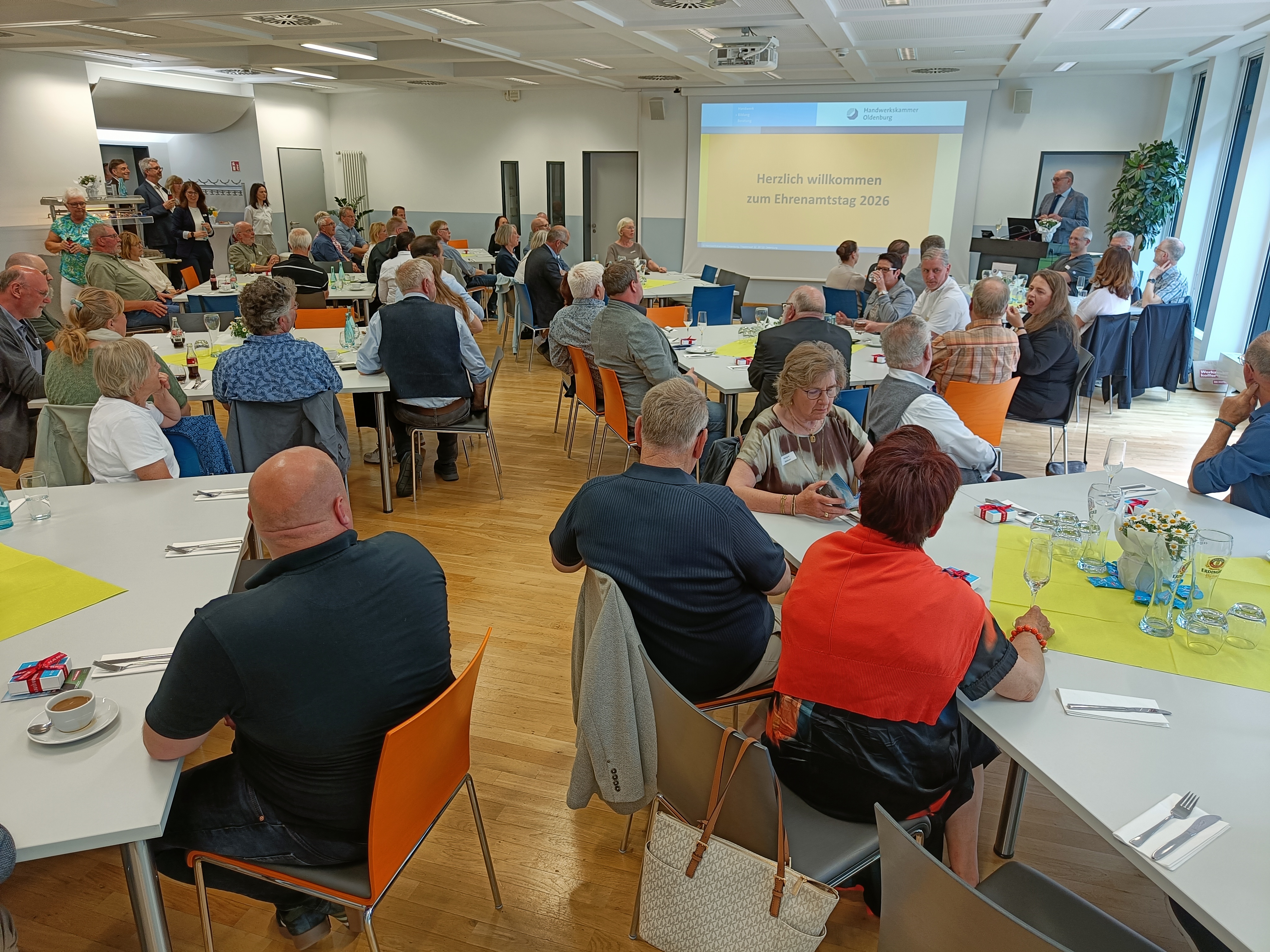 KI generiert: Eine Gruppe von Menschen sitzt in einem Veranstaltungsraum und nimmt an einer Ehrungsveranstaltung mit einer Projektionsleinwand teil.
