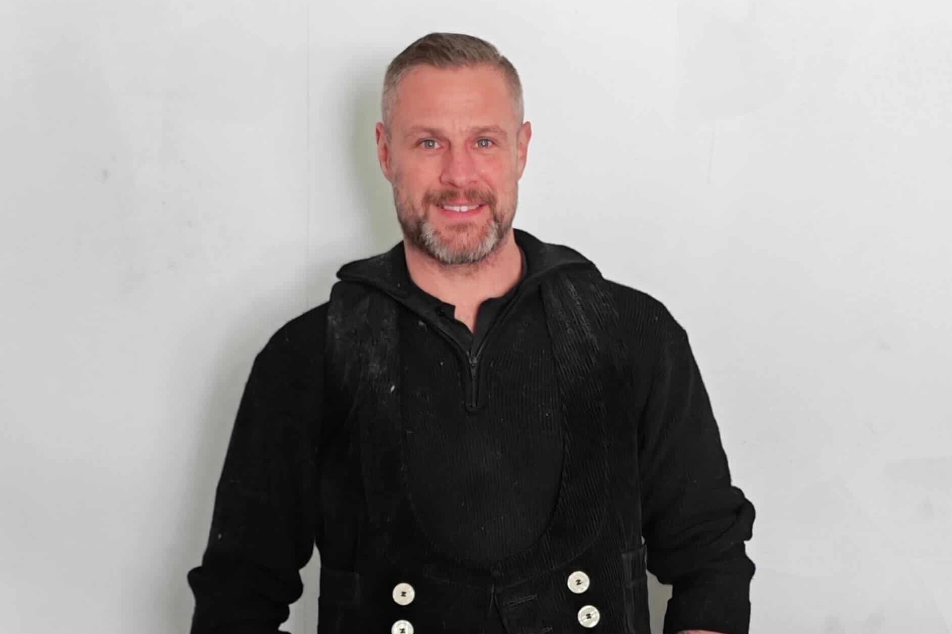 KI generiert: Ein Mann lächelt vor einem neutralen Hintergrund in die Kamera.