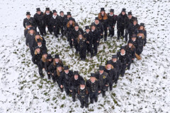 KI generiert: Eine Gruppe von Schornsteinfegern steht im Schnee in einer Herzform.