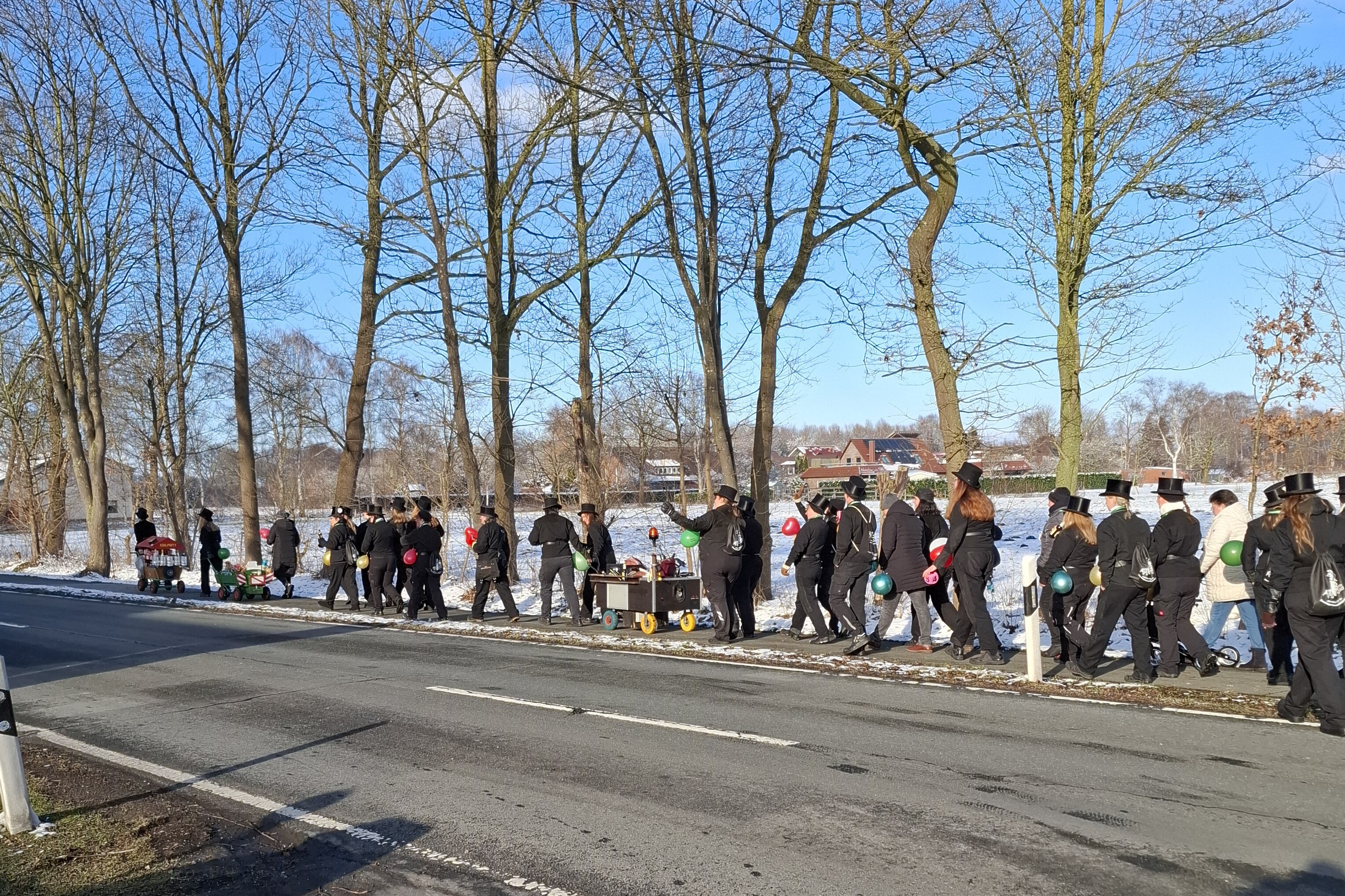 KI generiert: Eine Gruppe von Menschen mit Hüten zieht mit Handkarren auf einem winterlichen Bürgersteig entlang einer Straße.