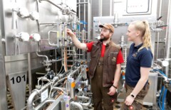 KI generiert: Zwei Personen arbeiten an einer komplexen technischen Anlage mit vielen Rohren und Ventilen.