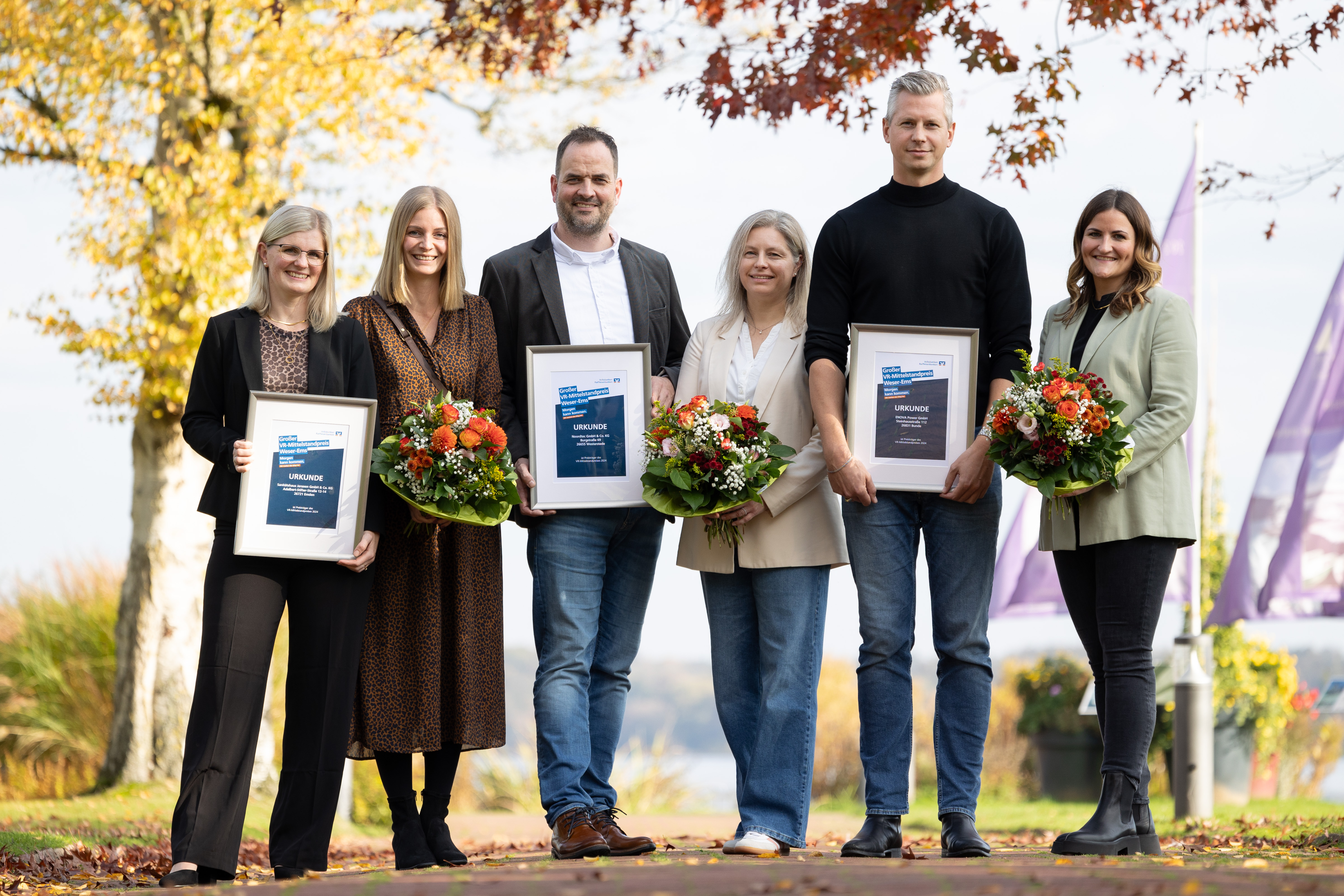 KI generiert: Mehrere Menschen posieren im Freien mit Urkunden und Blumensträußen.