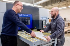 KI generiert: Zwei Männer arbeiten lächelnd an einer Maschine in einer Werkstatt.