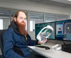 KI generiert: Ein Mann sitzt an einem Schreibtisch mit zwei Monitoren und hält ein Virtual-Reality-Headset.