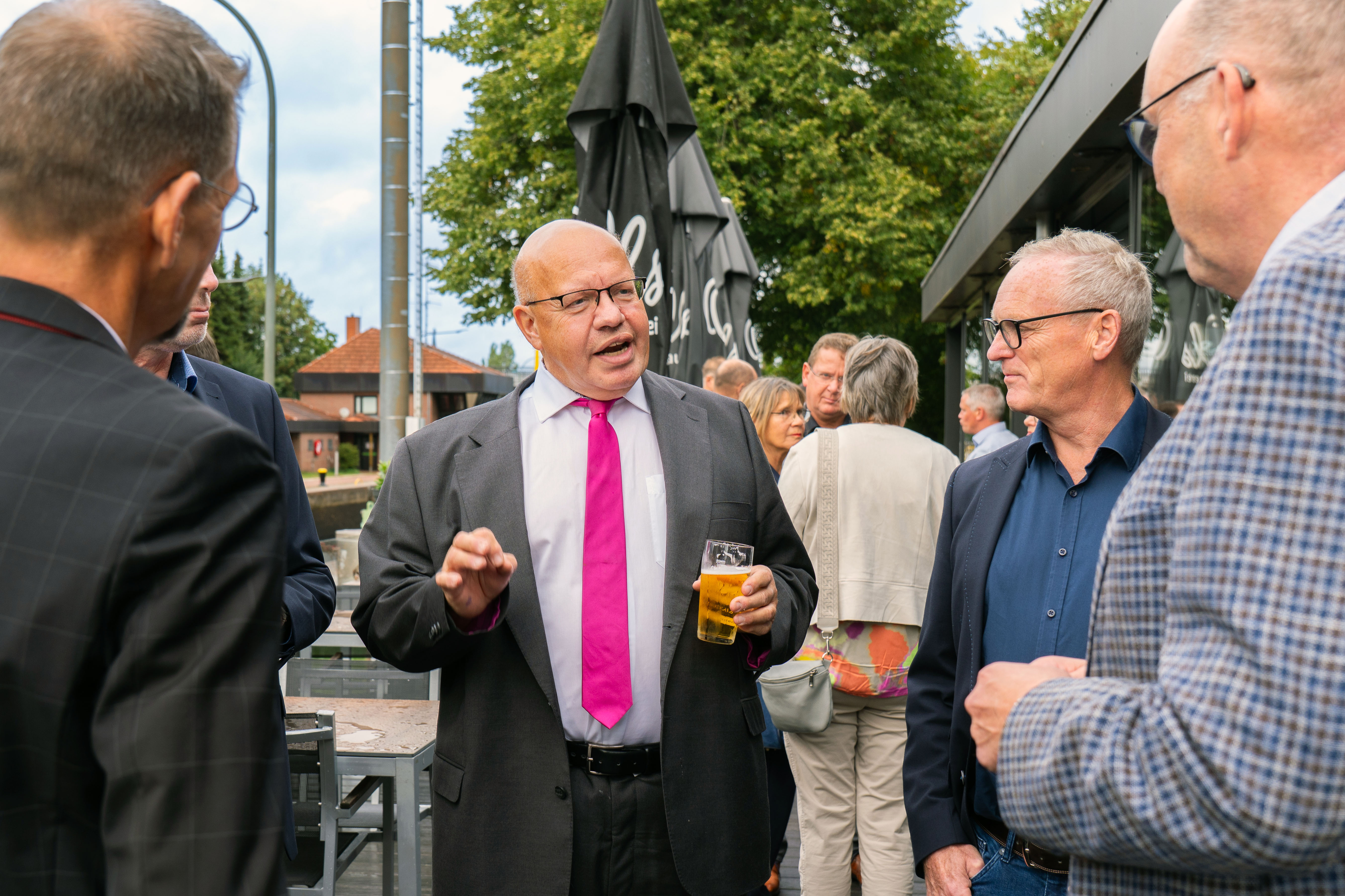 KI generiert: Das Bild zeigt eine Gruppe von Männern, die sich im Freien unterhalten und dabei Getränke in den Händen halten.