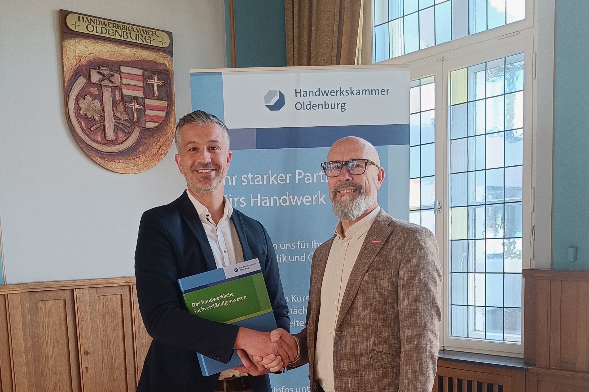 KI generiert: Zwei Männer stehen lächelnd vor einem Schild der Handwerkskammer Oldenburg und halten ein Zertifikat.