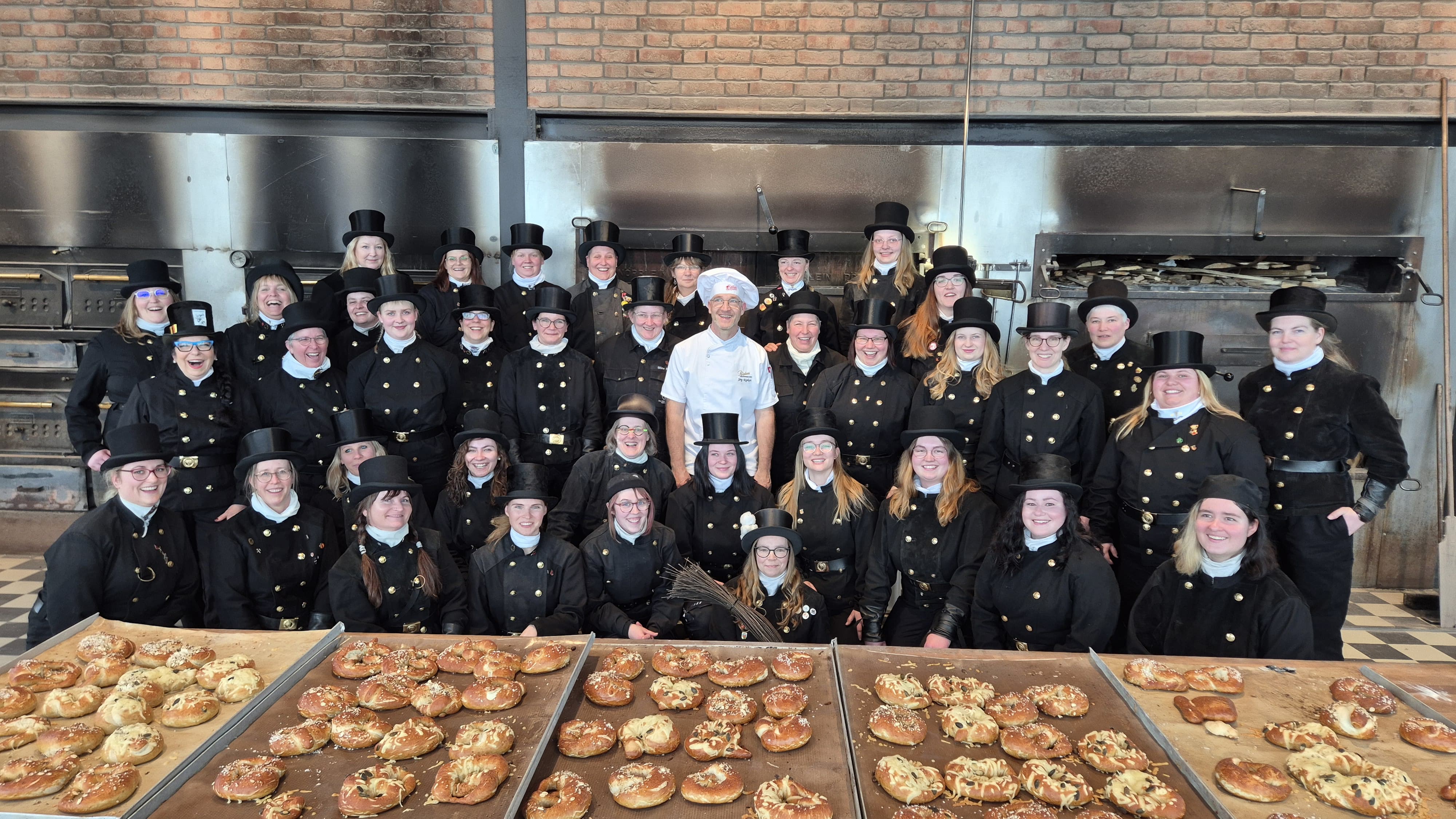 KI generiert: Eine Gruppe von Menschen in schwarzen Uniformen und ein Bäcker posieren vor Öfen und frisch gebackenem Gebäck.