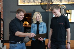 KI generiert: Drei Personen stehen zusammen in einem Raum und schauen gemeinsam auf ein Tablet.