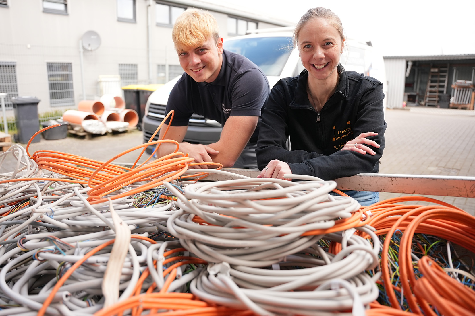 KI generiert: Zwei Personen stehen draußen hinter einem großen Haufen Kabel.