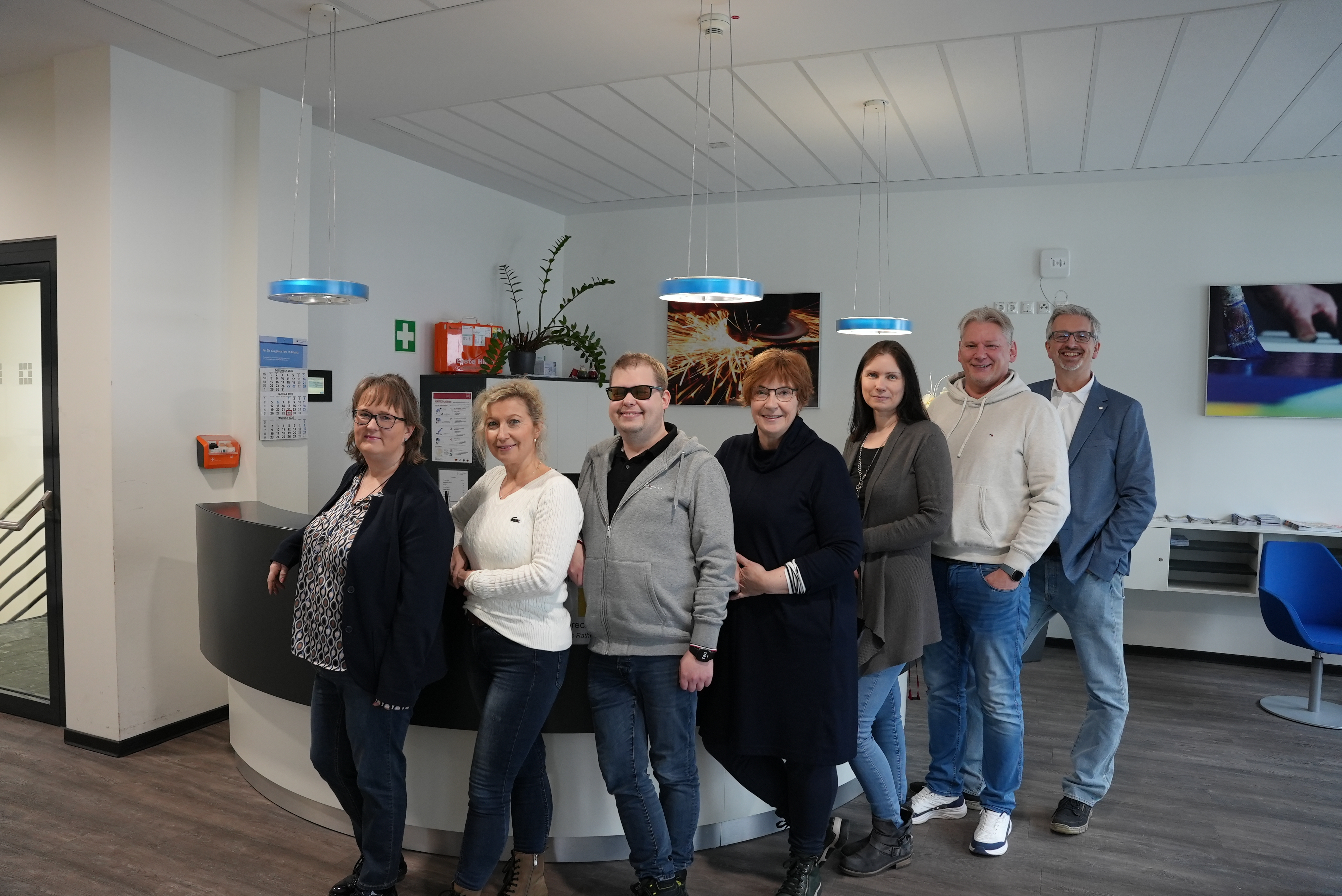 KI generiert: Eine Gruppe von sieben Personen steht lächelnd in einem modernen Büro vor einem Empfangstresen.