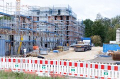 KI generiert: Das Bild zeigt eine Baustelle mit einem großen, im Bau befindlichen mehrstöckigen Gebäude, umgeben von Gerüsten und Baumaterialien.